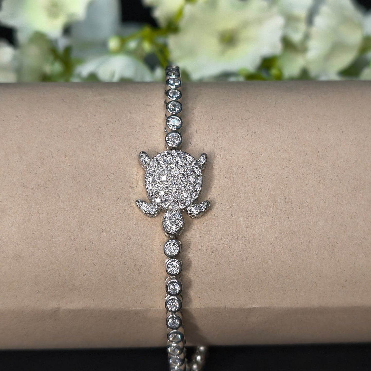 Silver bracelet with a diamond flower clasp on a wrist, with flowers in the background