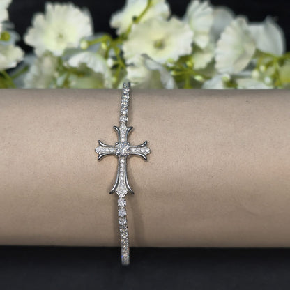 Silver cross bracelet on a wrist with white flowers in the background
