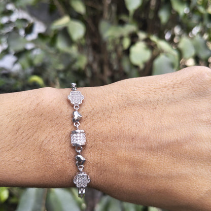 Silver bracelet with charms on a wrist against a blurred green background