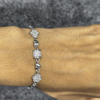 Silver bracelet with heart and floral designs on a wrist against a gray background