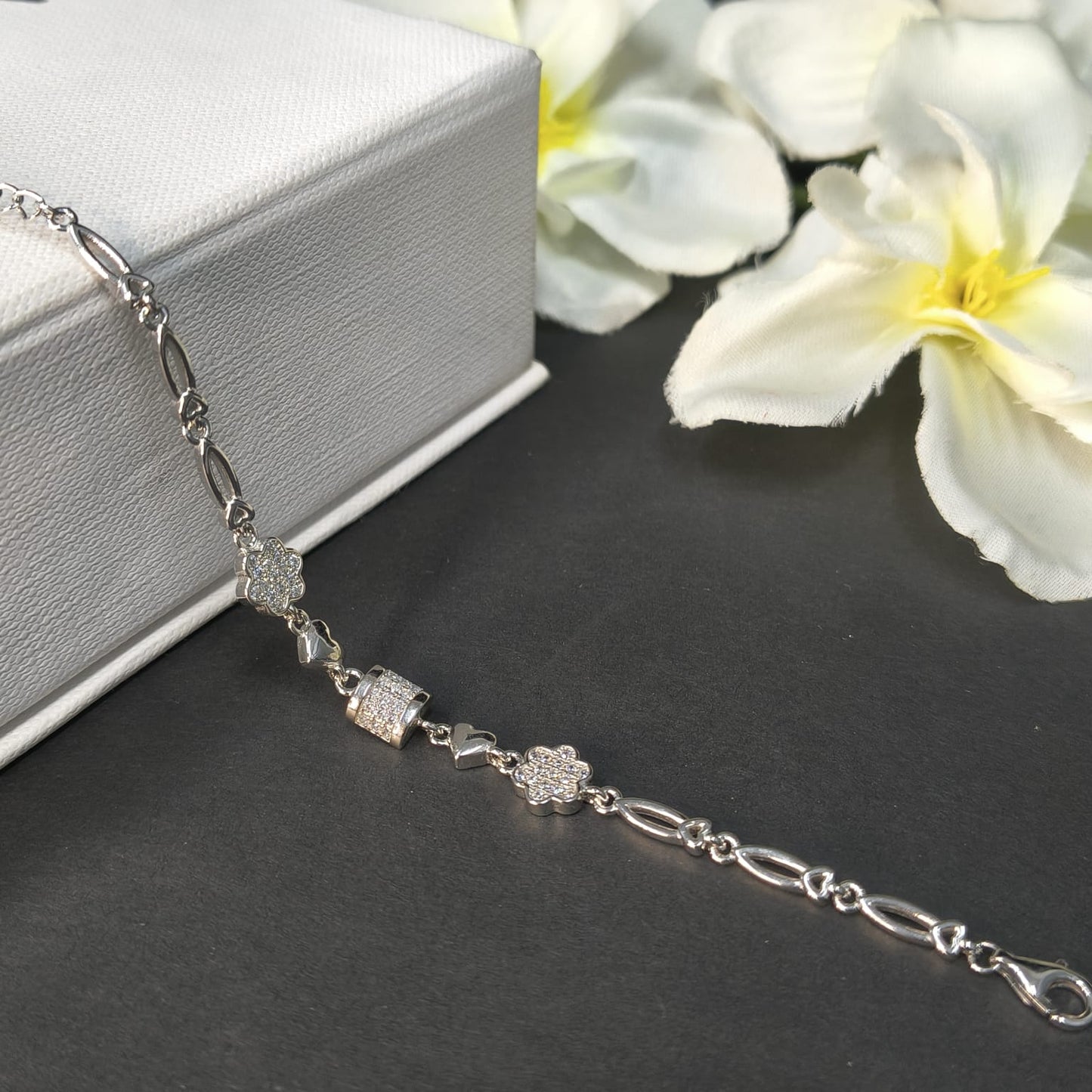 Silver bracelet with floral designs on a dark surface with white flowers in the background