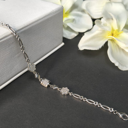Silver bracelet with floral designs on a dark surface with white flowers in the background