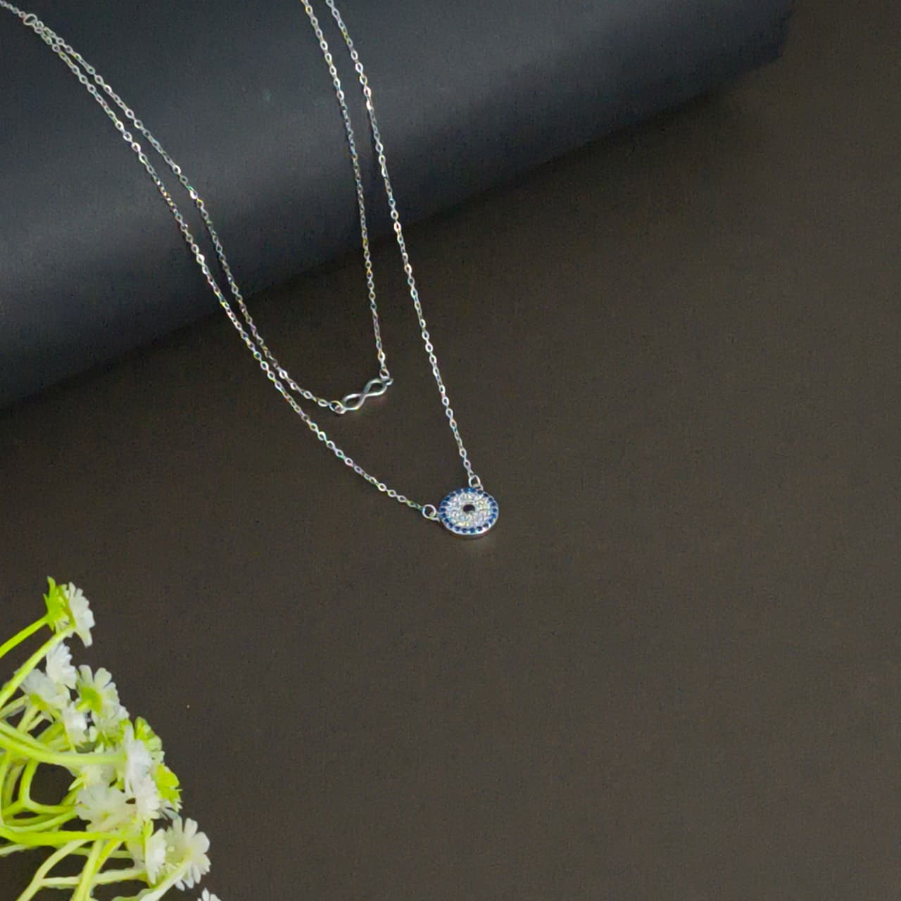 Silver necklace with a small pendant on a dark surface with green flowers.