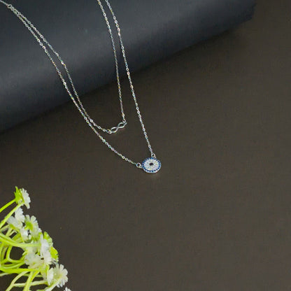Silver necklace with a small pendant on a dark surface with green flowers.