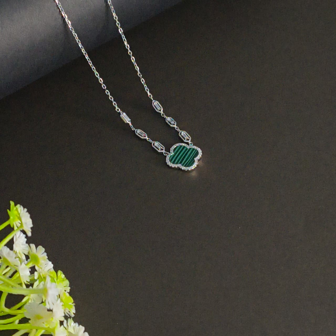 Necklace with a green pendant on a dark surface with white flowers.