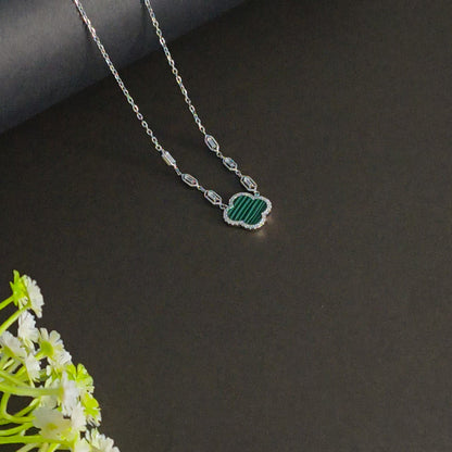 Necklace with a green pendant on a dark surface with white flowers.