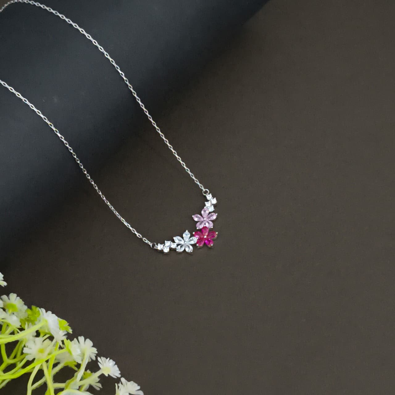 Silver necklace with floral pendants on a dark surface with flowers.