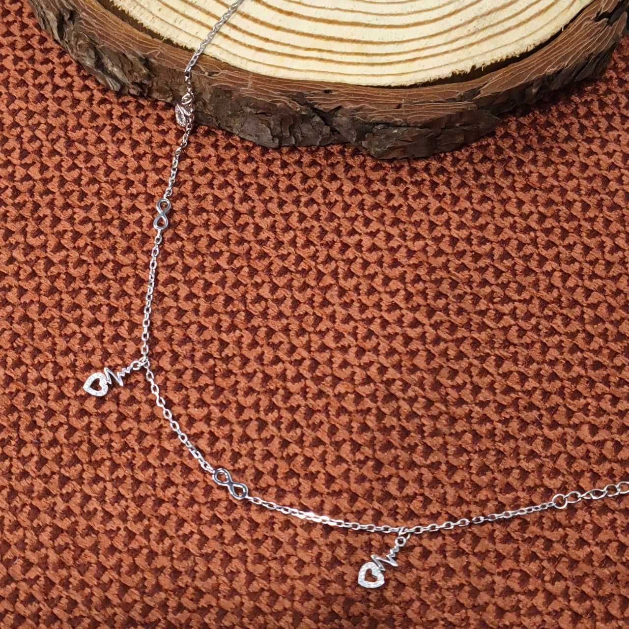 Silver chain bracelet with a heart charm on a textured brown surface.