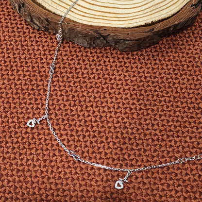 Silver chain bracelet with a heart charm on a textured brown surface.