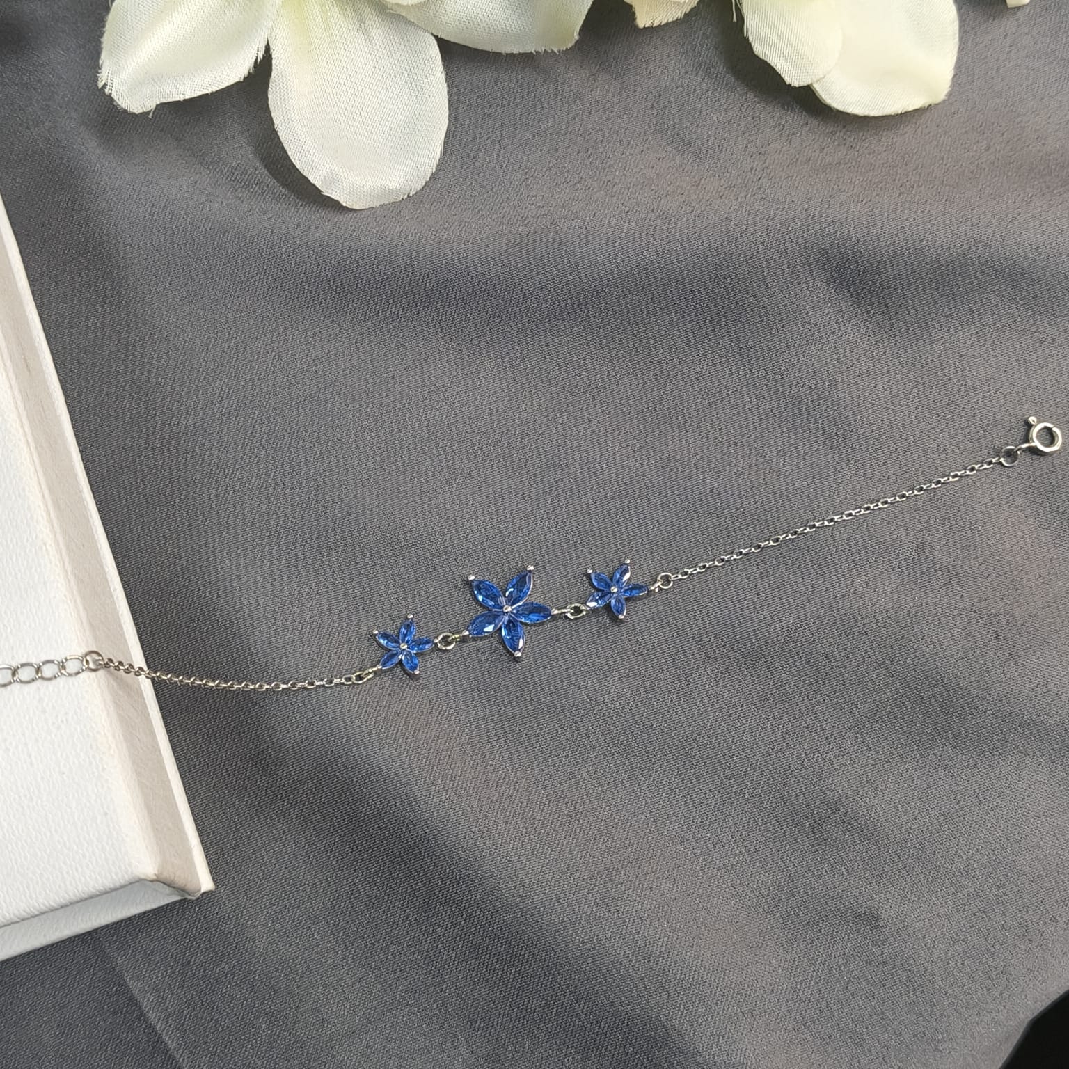 Silver bracelet with blue star-shaped charms on a gray surface with white flowers.