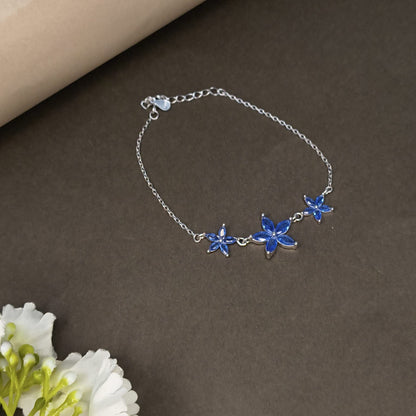 Silver bracelet with blue flower charms on a brown surface with white flowers.