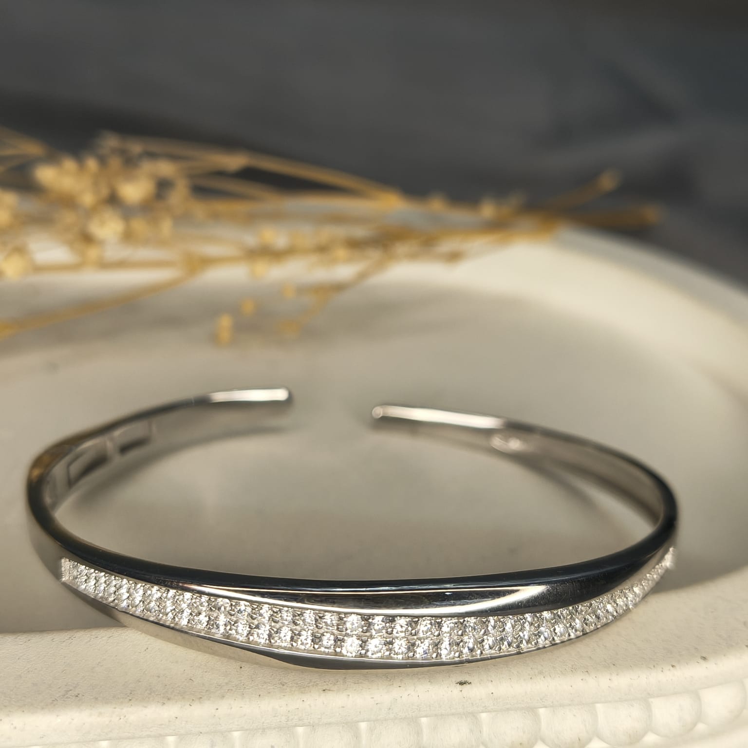Silver bracelet with small diamonds on a textured surface with dried plants in the background