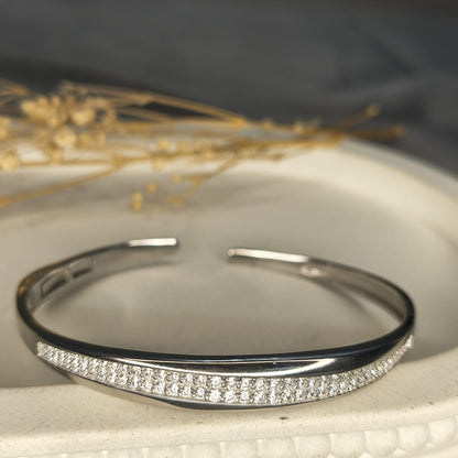 Silver bracelet with small diamonds on a textured surface with dried plants in the background