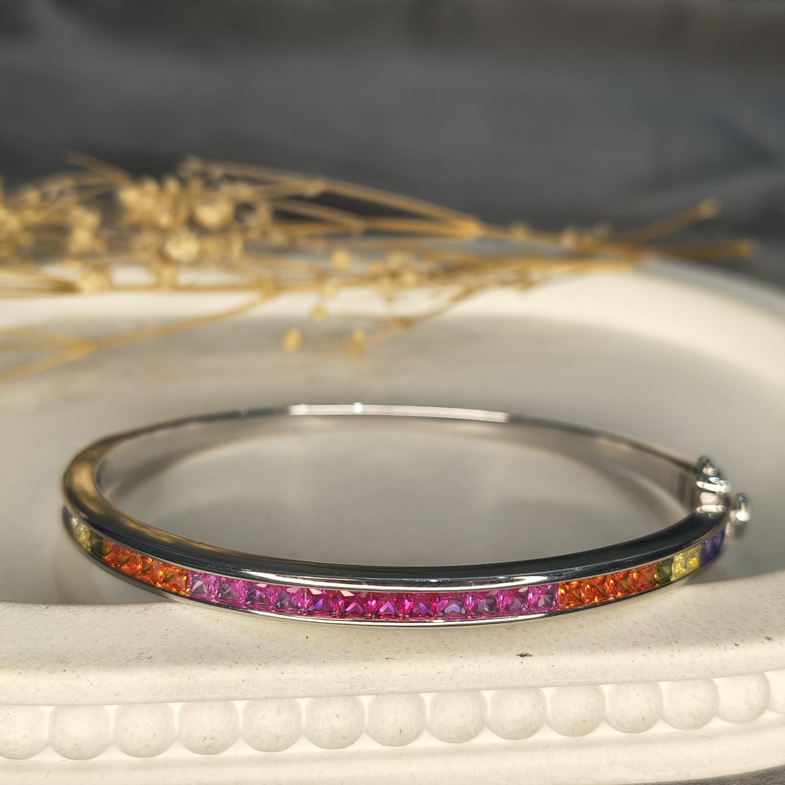 Silver bracelet with colorful stones on a textured white surface with blurred natural elements in the background