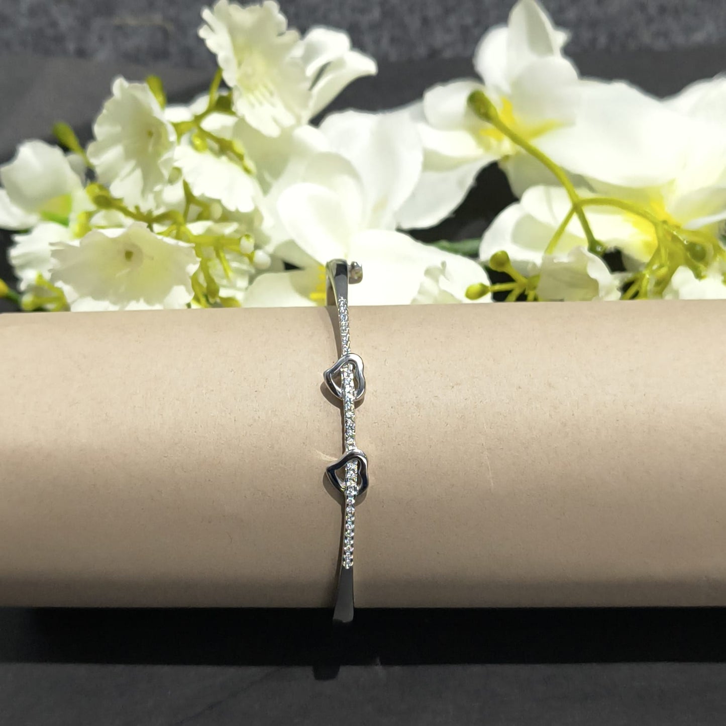 Silver bracelet on a beige cylindrical stand with white flowers in the background