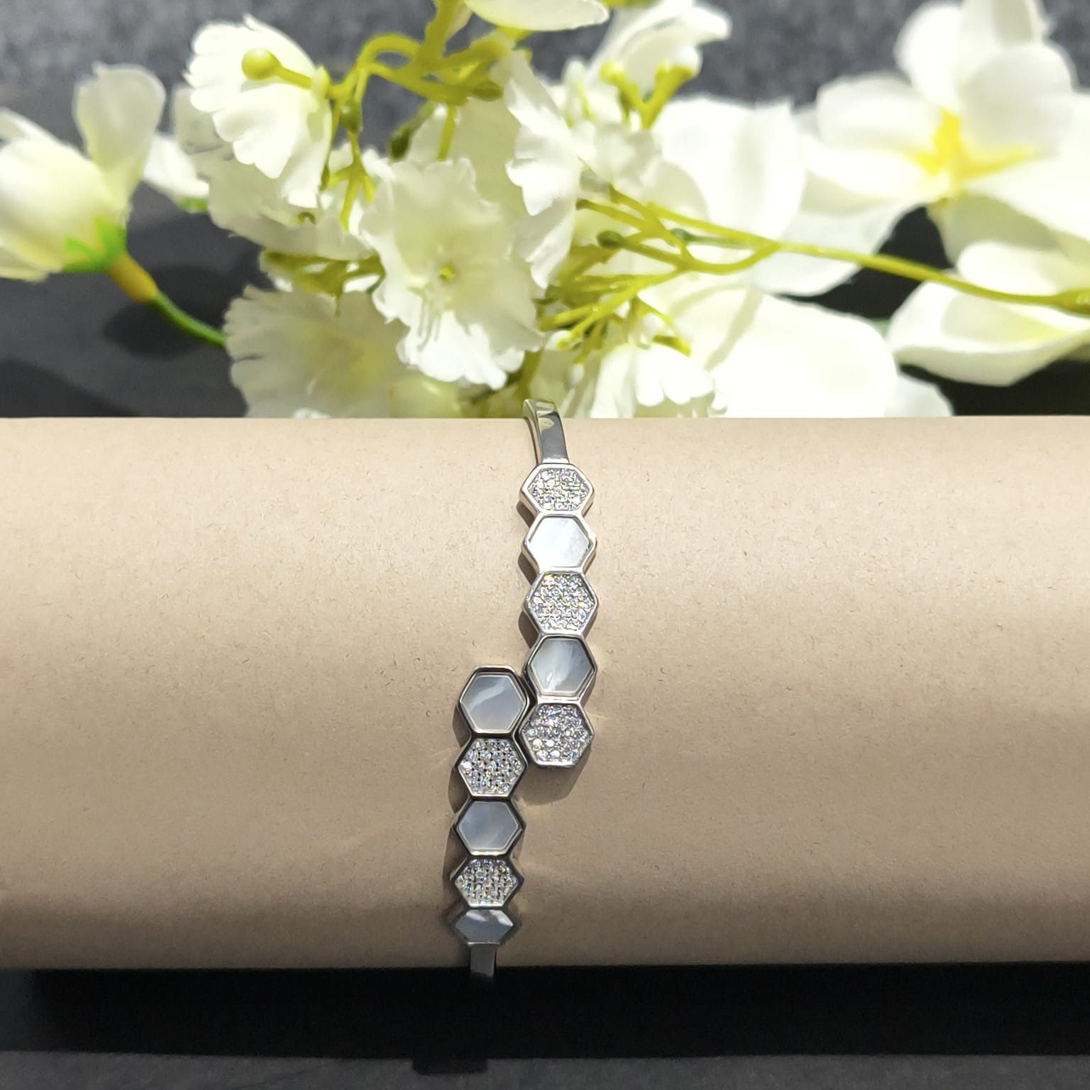 Silver bracelet with hexagonal pattern on a beige surface with white flowers in the background
