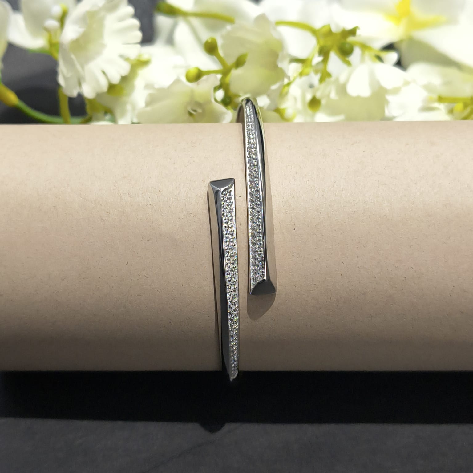 Silver bracelet on a cylindrical object with white flowers in the background