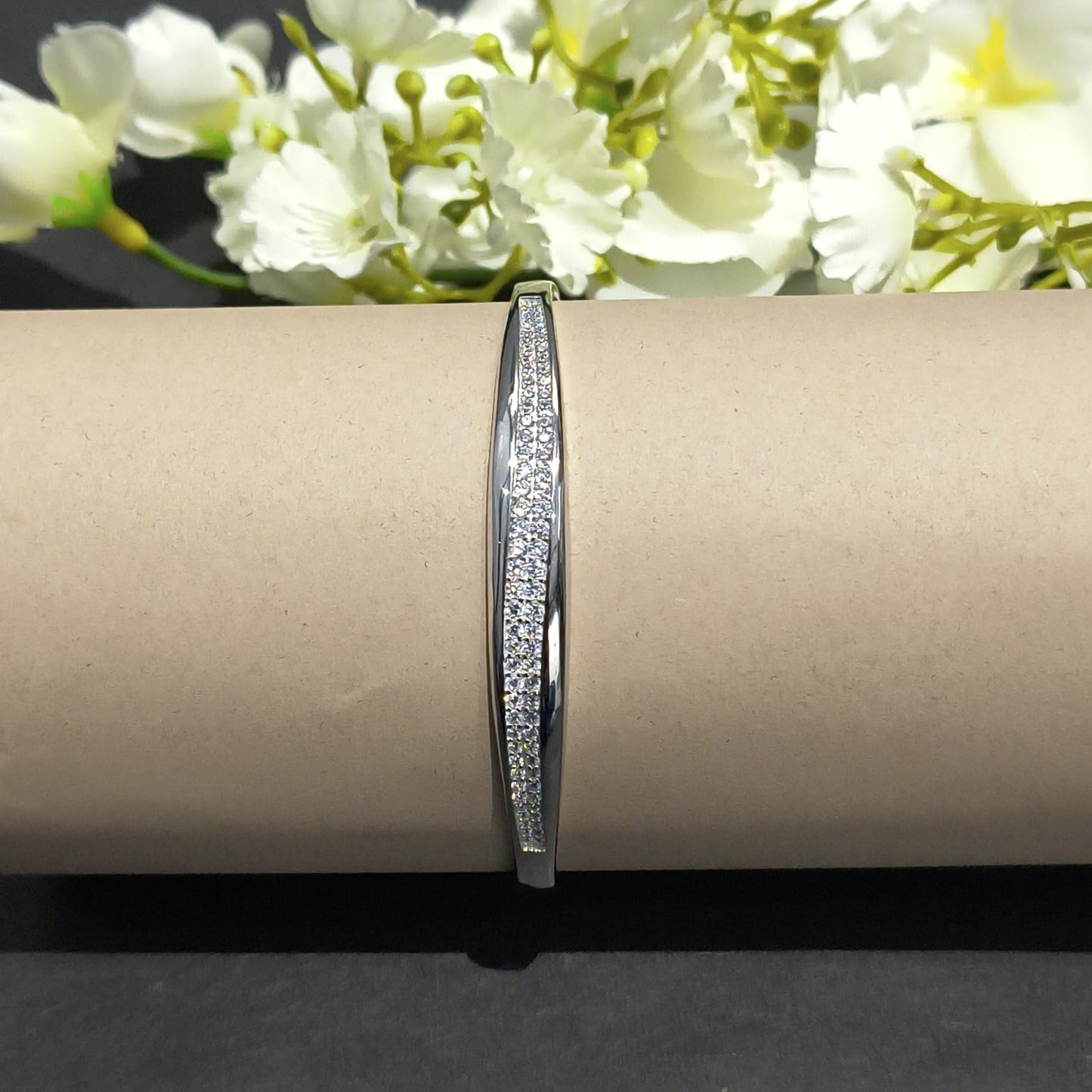 Silver bracelet on a cardboard roll with white flowers in the background