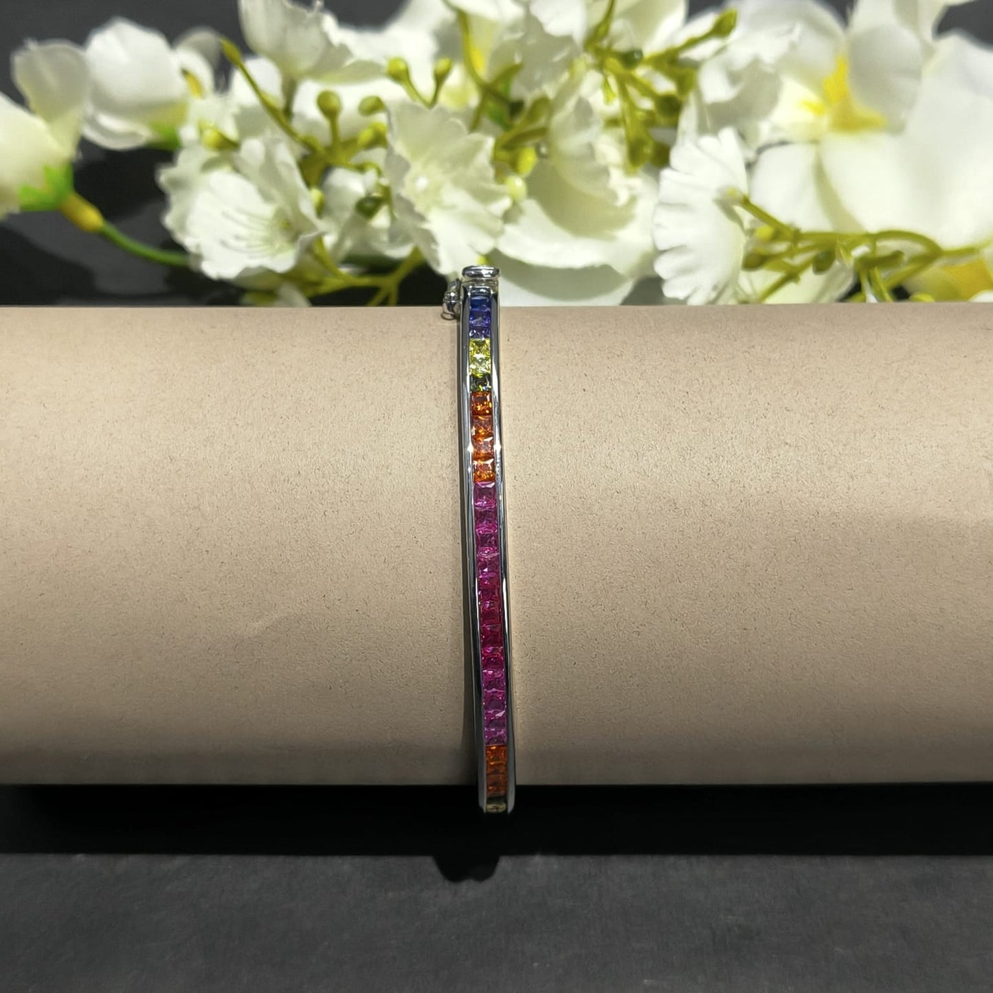 Multicolored gemstone bracelet on a beige surface with white flowers in the background
