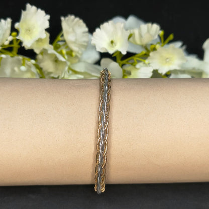 Gold braided bracelet on a person's wrist with white flowers in the background