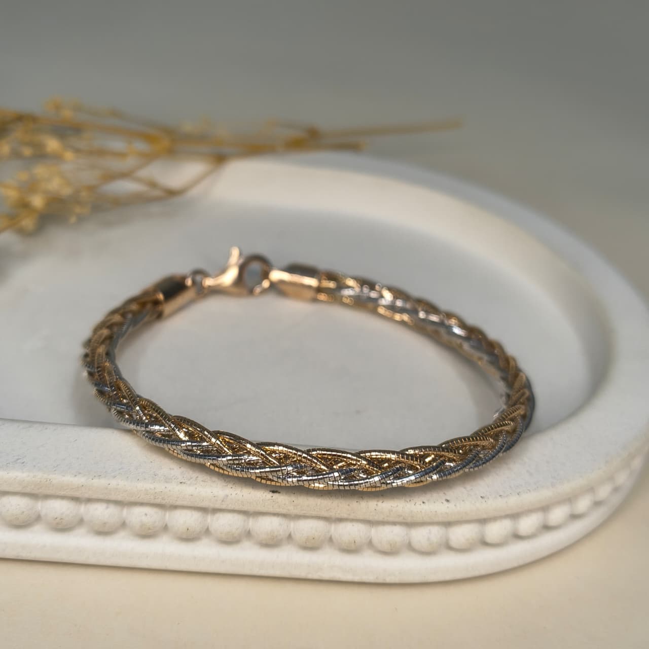 Gold bracelet on a white jewelry dish with a blurred background