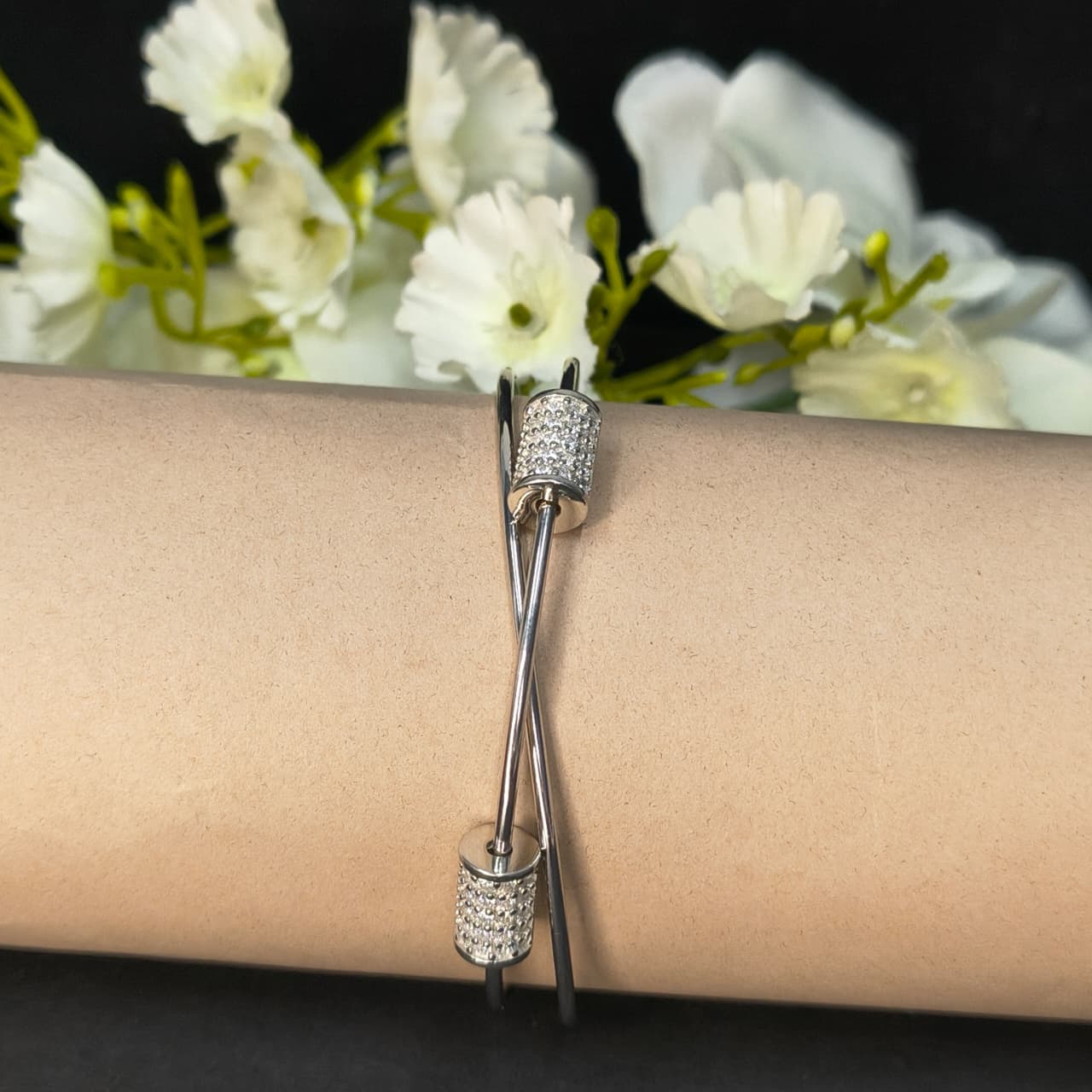Silver bracelet on a wrist with white flowers in the background