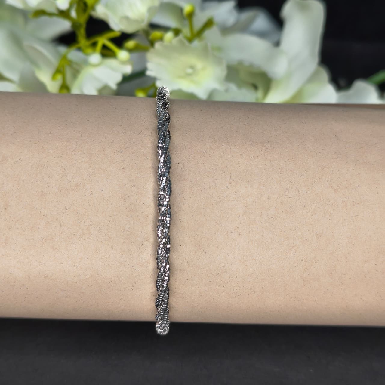 Silver bracelet on a wrist with a blurred floral background