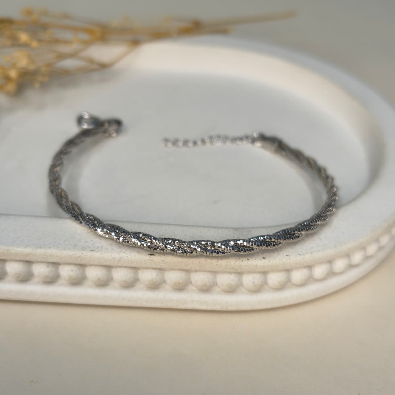 Silver bracelet on a decorative white surface with dried flowers.