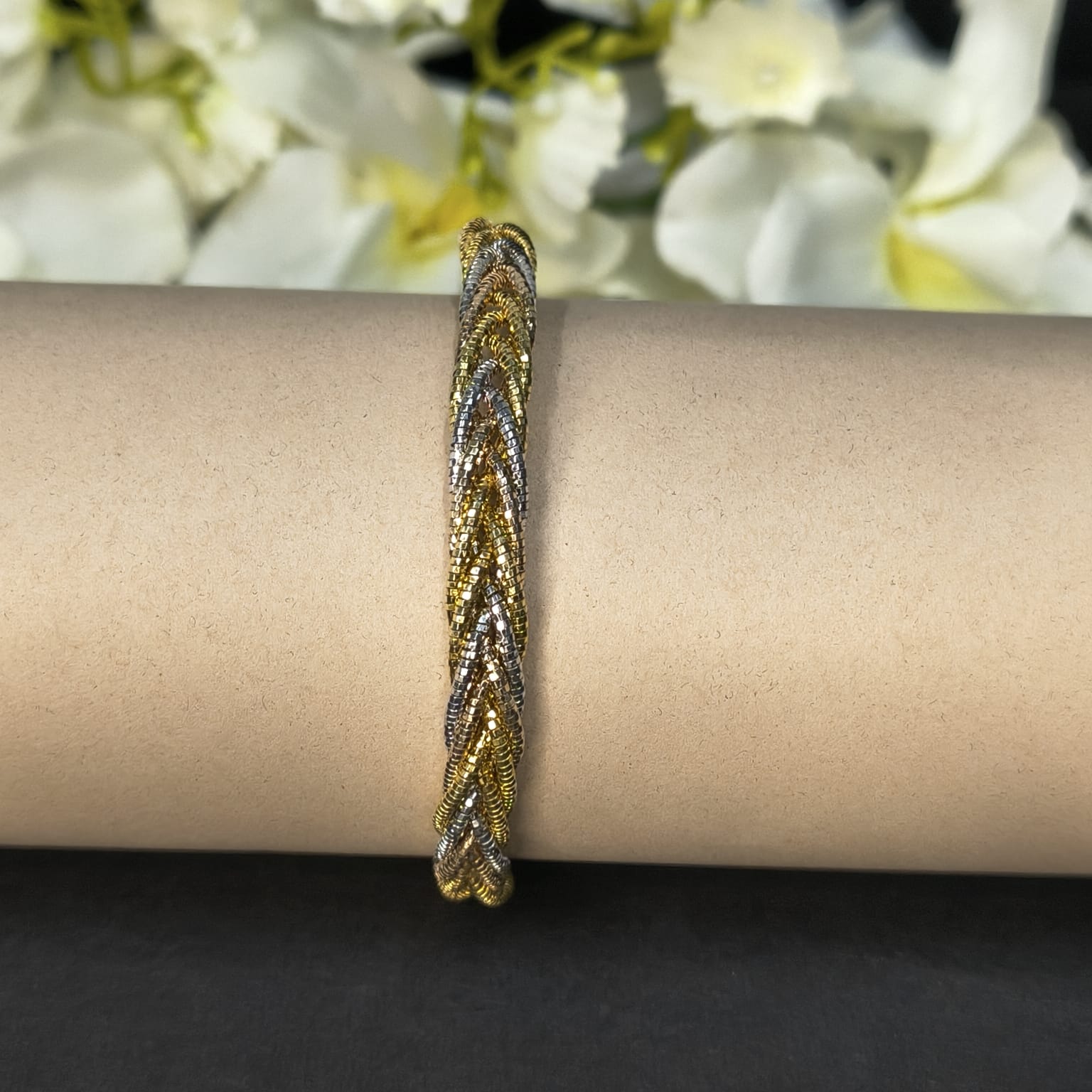 Gold and silver braided bracelet on a wrist with a blurred floral background