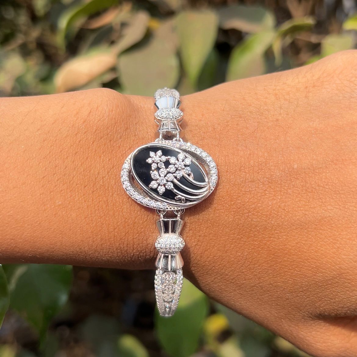 Silver bracelet with black stone and floral design on a wrist against a blurred green background