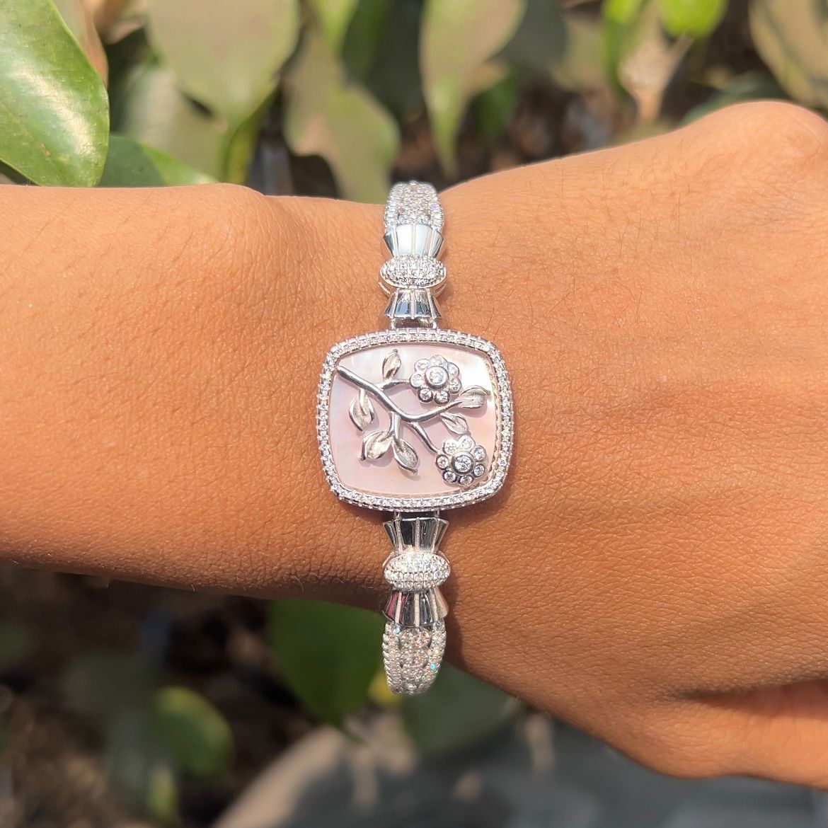 Silver bracelet with floral design on a wrist against a natural background