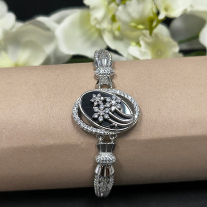 Silver bracelet with black center and floral design on a wrist, with white flowers in the background.