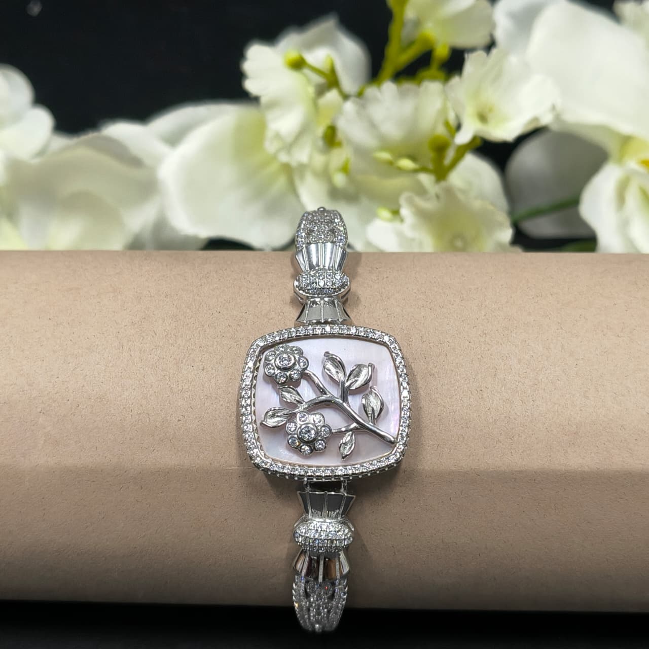 Silver bracelet with intricate design on a wrist against a floral background