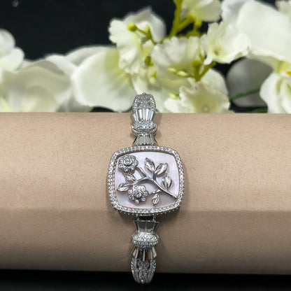 Silver bracelet with intricate design on a wrist against a floral background