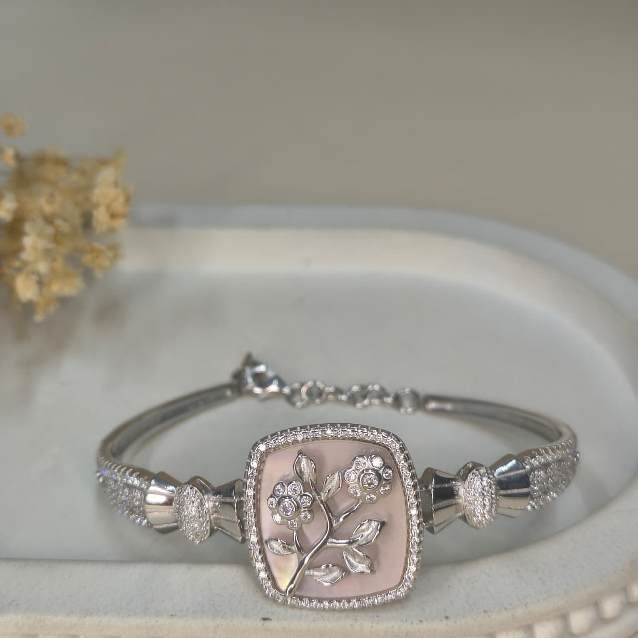 Silver bracelet with floral design on a white surface