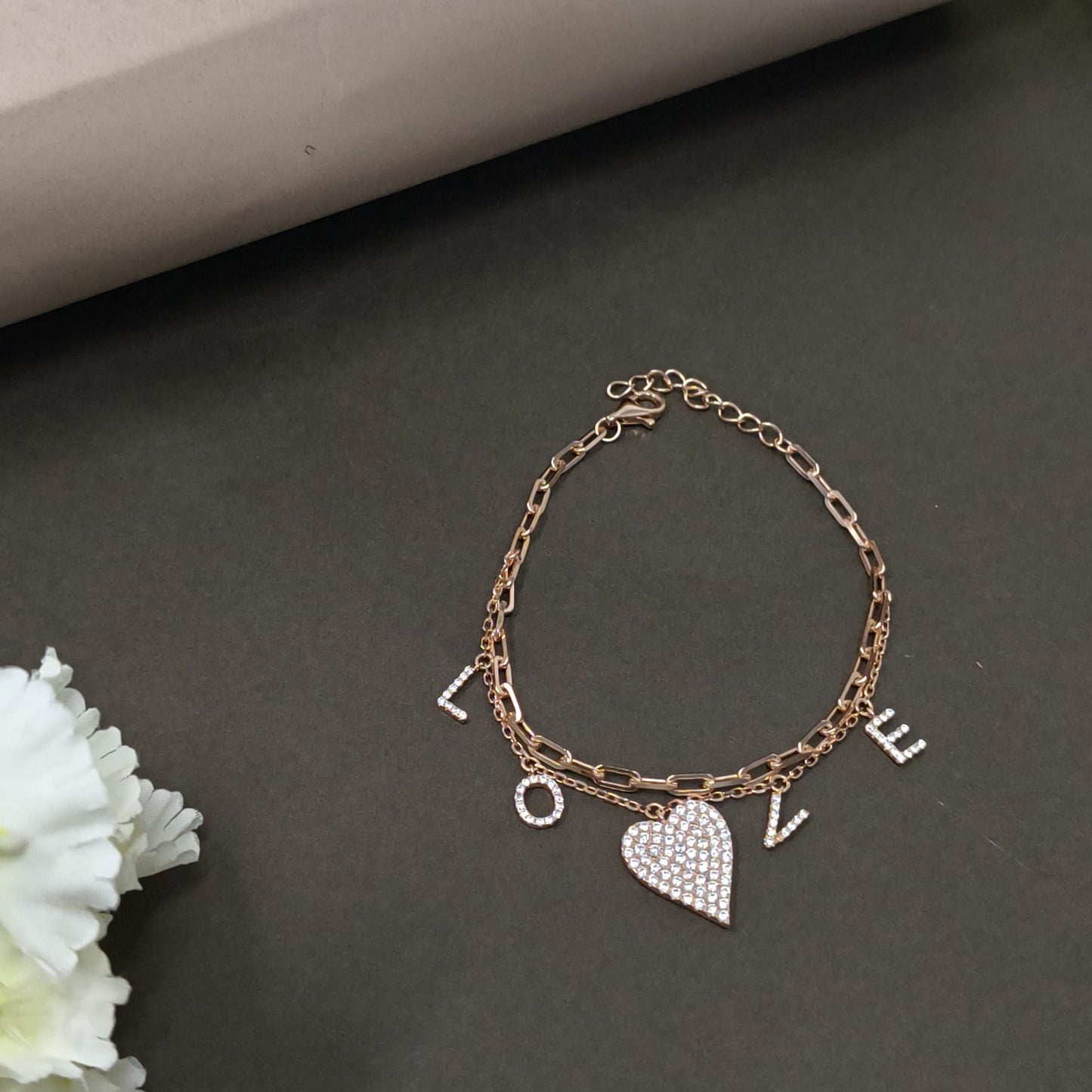 Bracelet with heart and letter charms on a dark surface with a white flower.