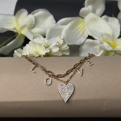 Gold bracelet with heart charm on a beige surface with white flowers in the background