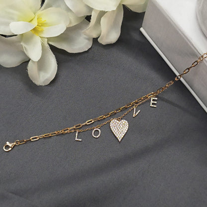 Gold bracelet with 'LOVE' charms on a gray surface with white flowers.