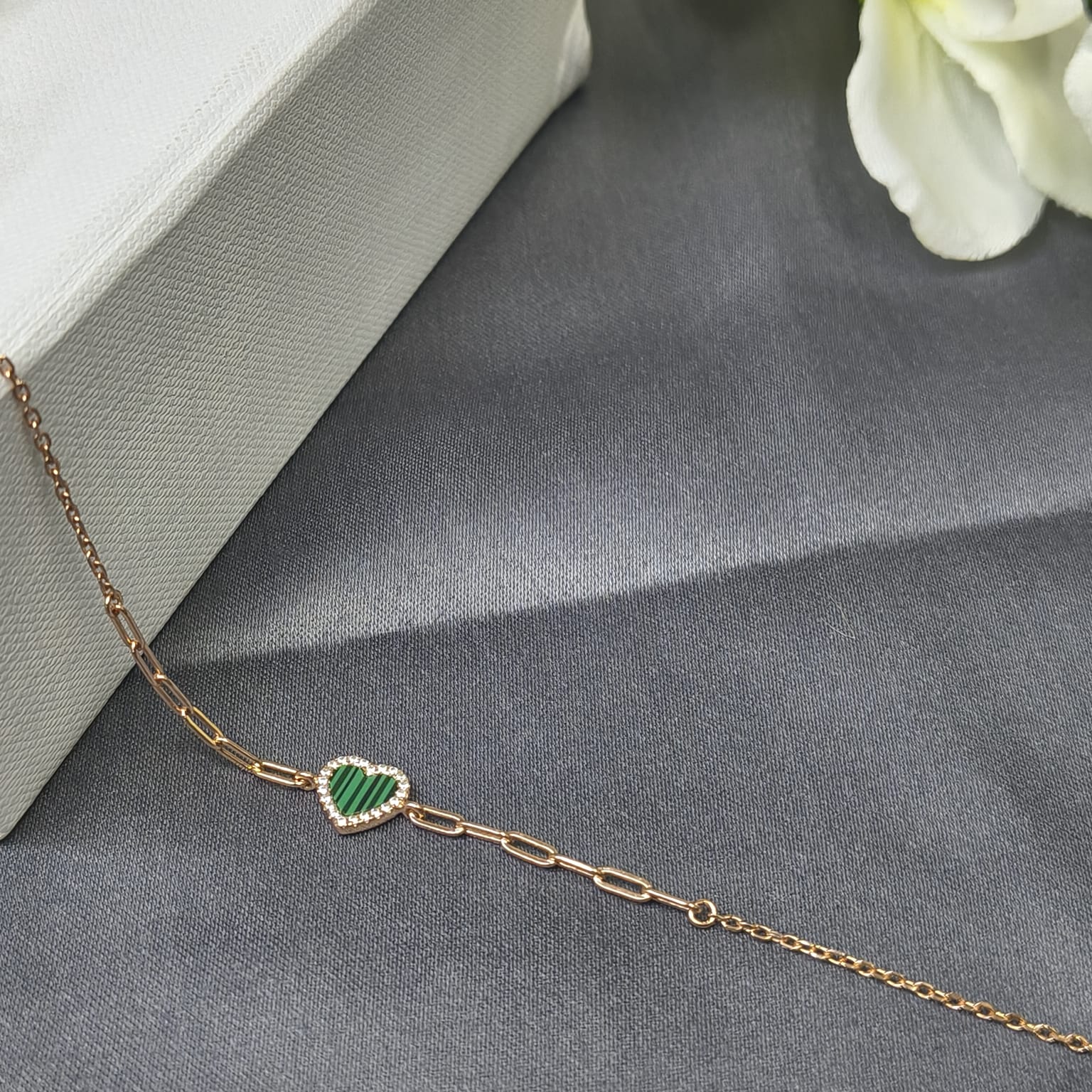 Gold bracelet with a green heart charm on a gray surface