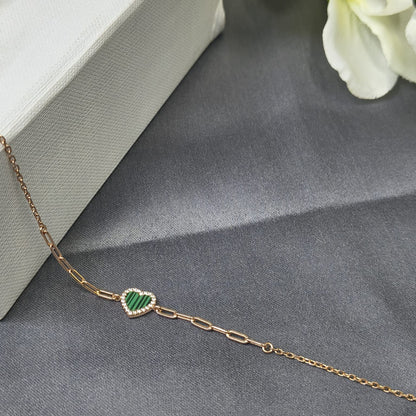 Gold bracelet with a green heart charm on a gray surface