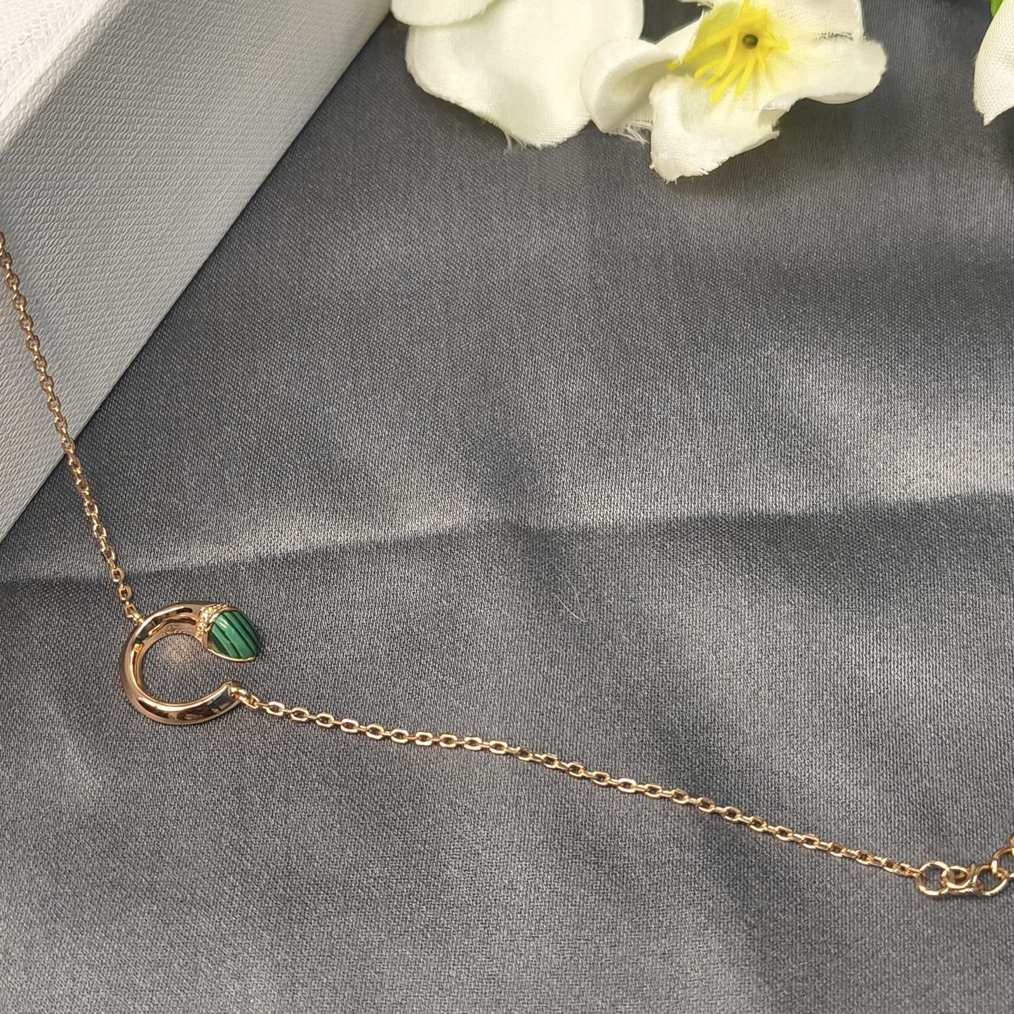 Gold necklace with a green gemstone on a gray surface with flowers in the background