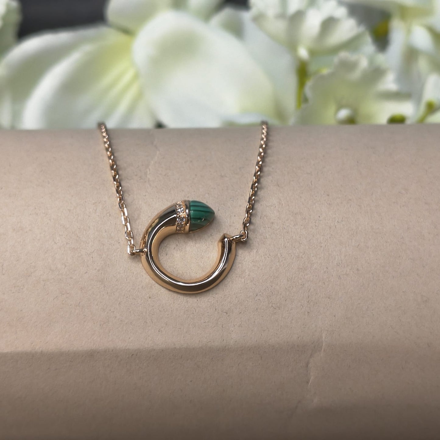 Gold necklace with a green pendant on a person's wrist against a floral background