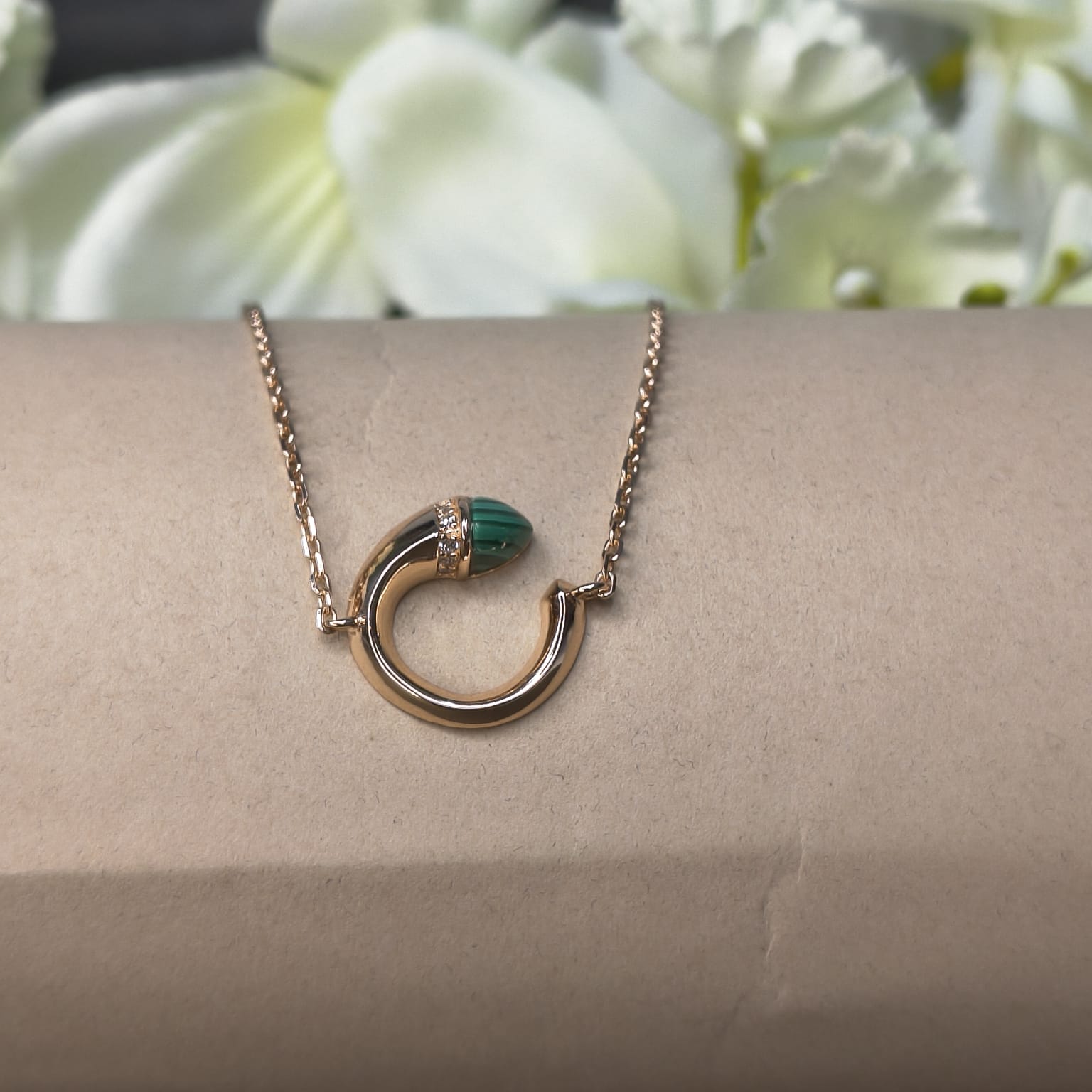Gold necklace with a green pendant on a person's wrist against a floral background