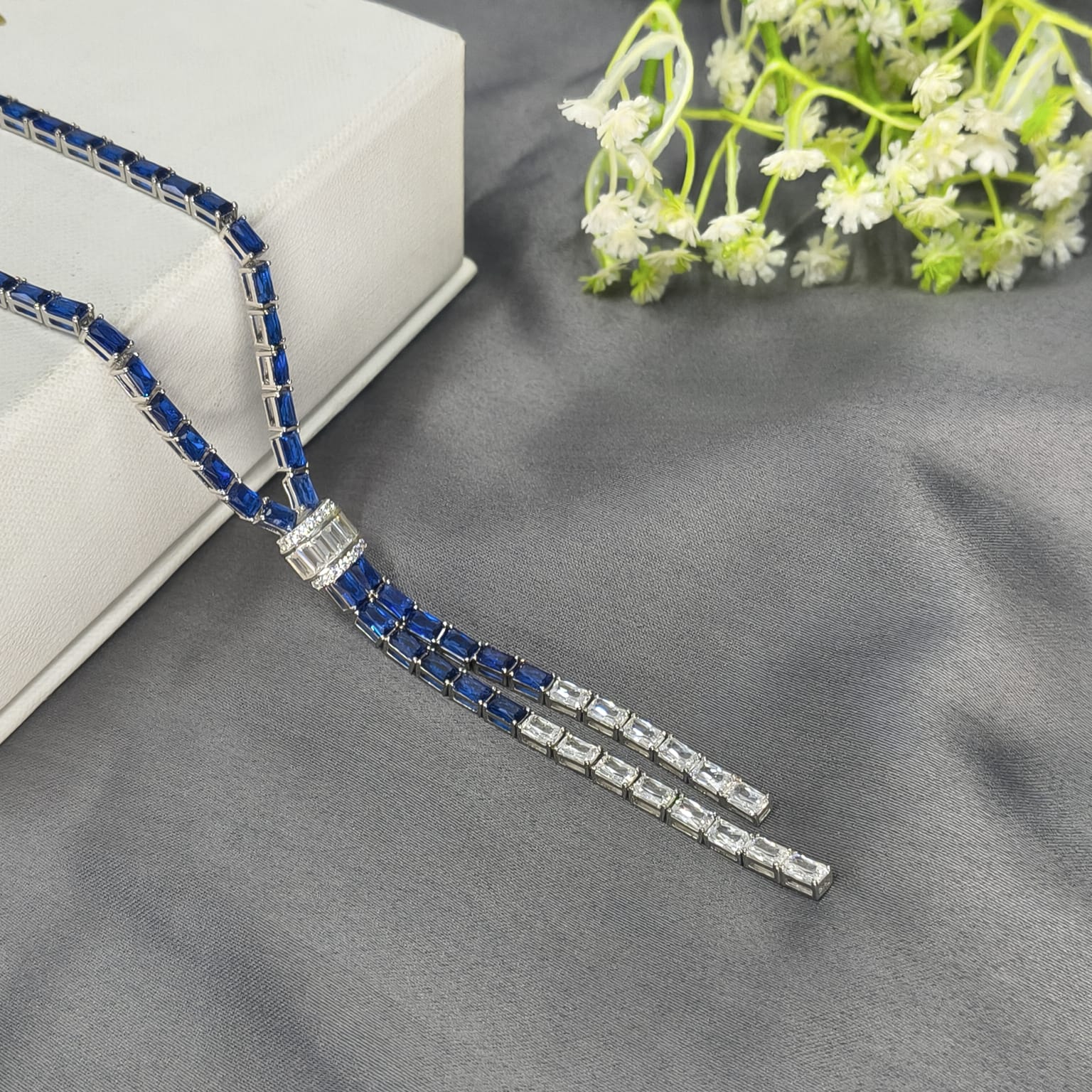 Silver and blue beaded necklace on a gray surface with white flowers in the background