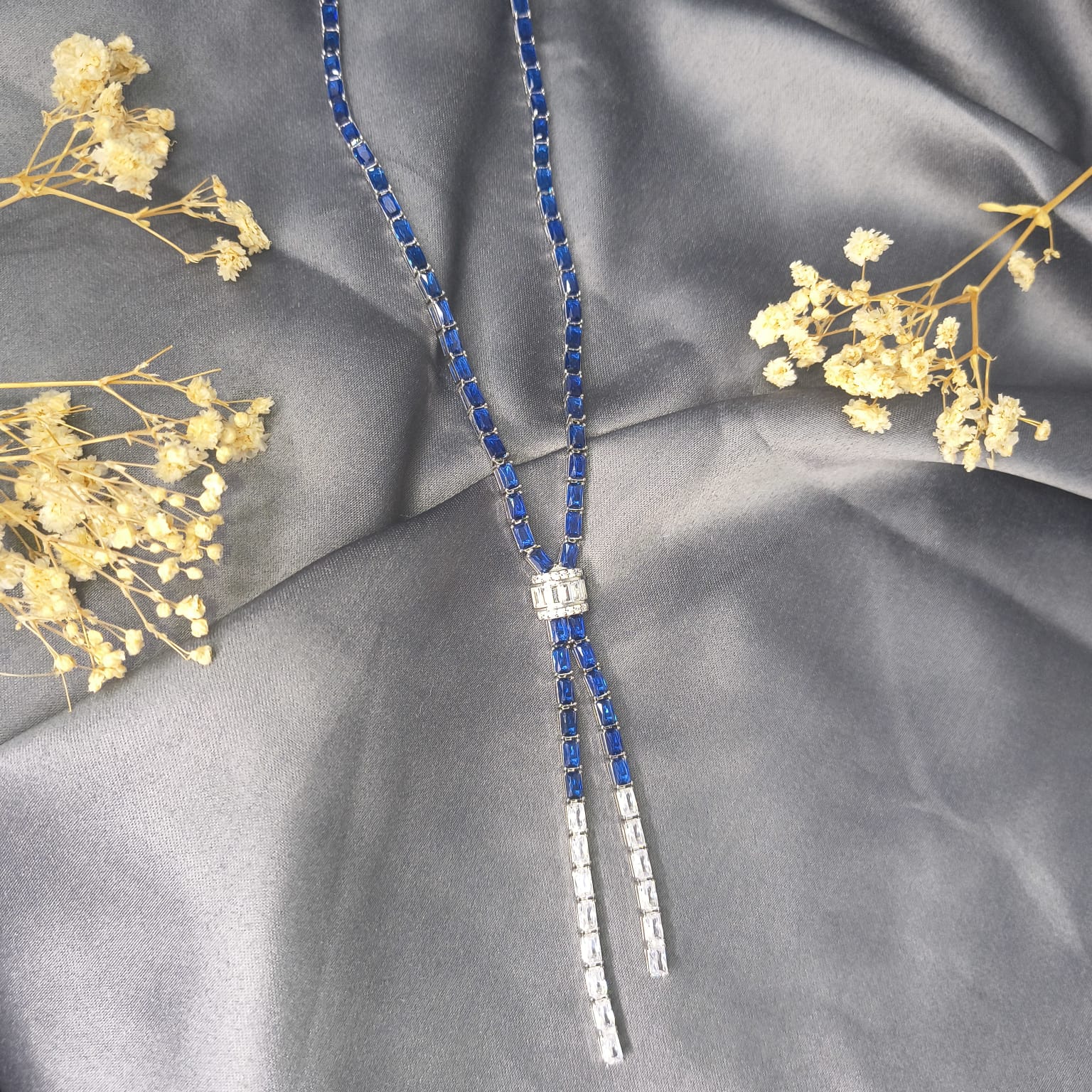 Necklace with blue and silver beads on a gray fabric background with dried flowers.