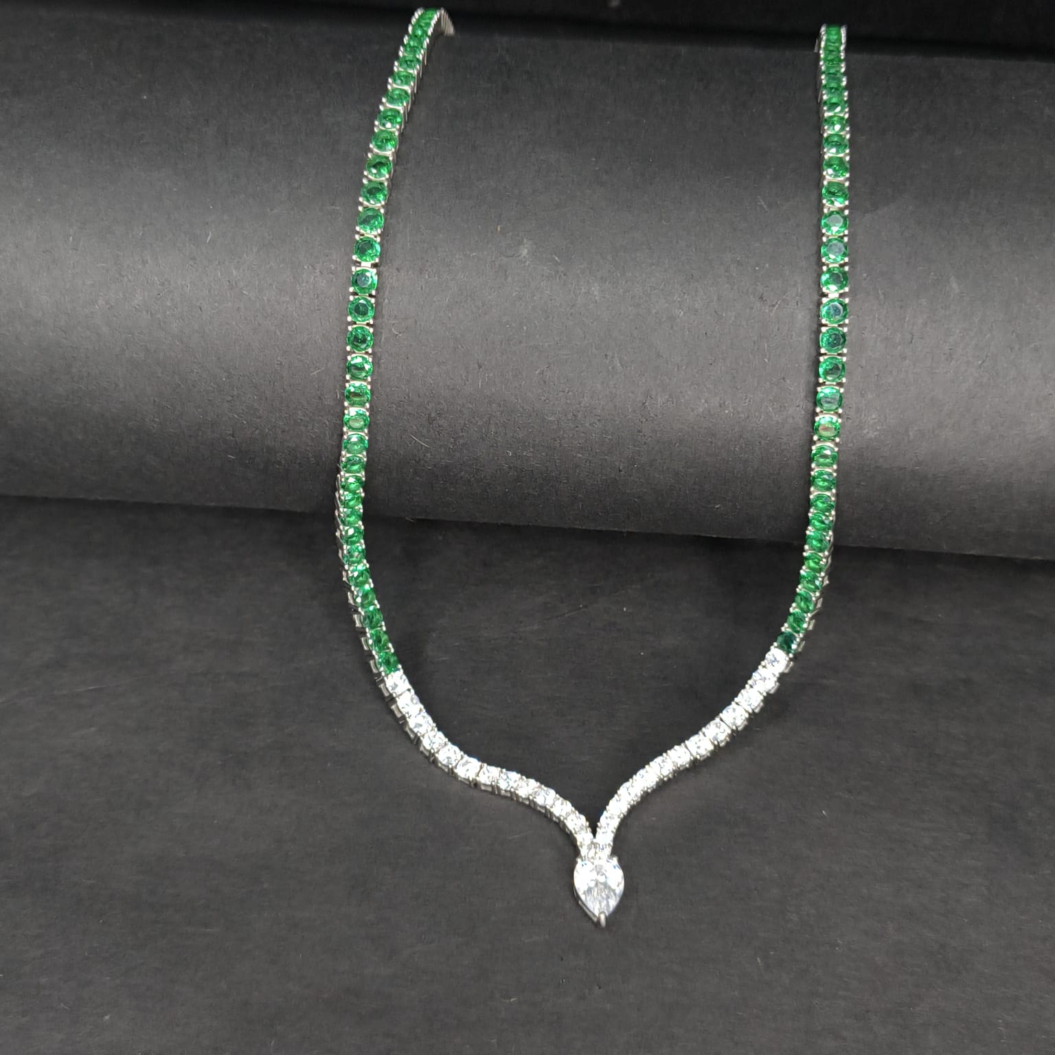 Necklace with green gemstones and a diamond pendant on a dark background