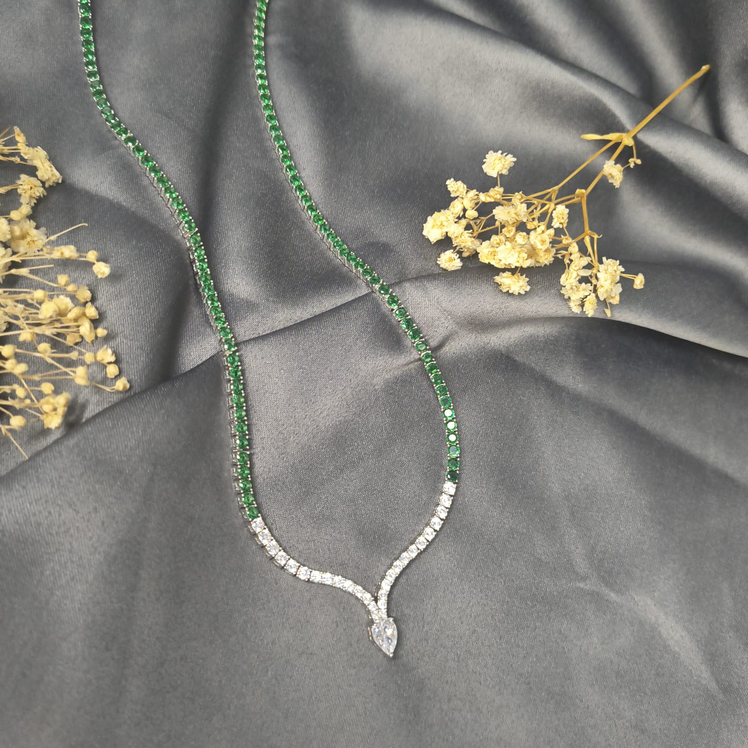 Green gemstone necklace with diamond pendant on gray fabric with dried flowers
