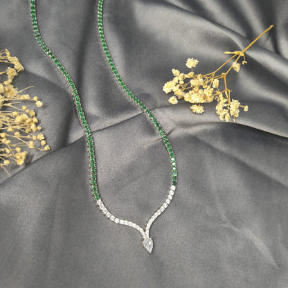 Green gemstone necklace with diamond pendant on gray fabric with dried flowers