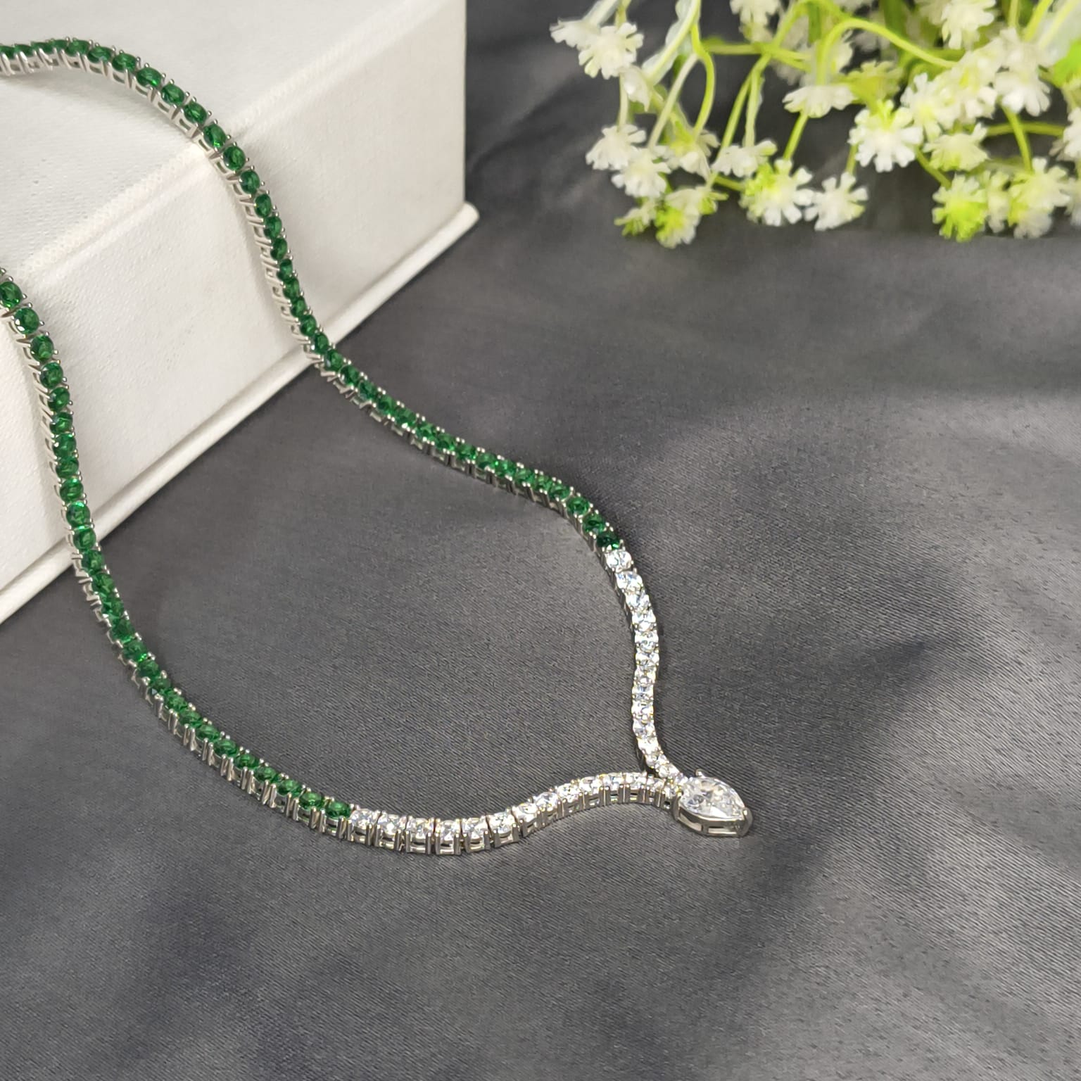 Emerald and diamond necklace on a gray surface with flowers in the background