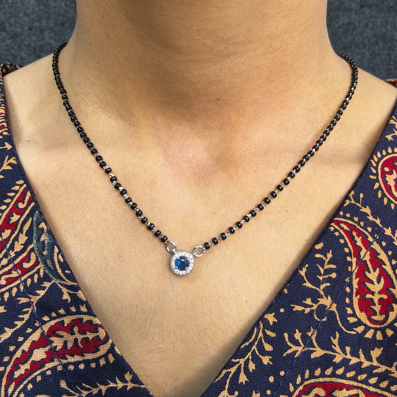 Necklace with a blue gemstone pendant on a person wearing a patterned garment.
